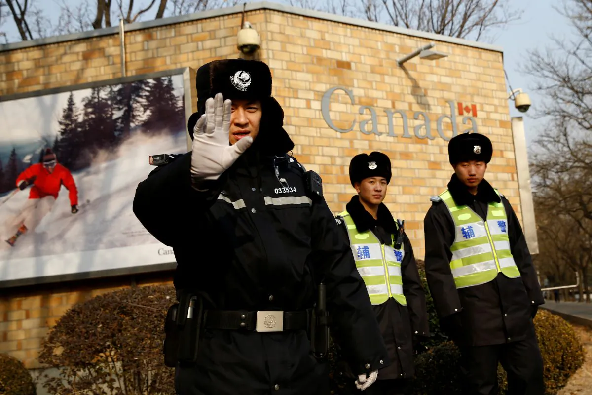 A police officer gestures at the photographer as security staff stand guard outside the Canadian embassy in Beijing, China, on Dec. 20, 2018.  (Thomas Peter/Reuters)