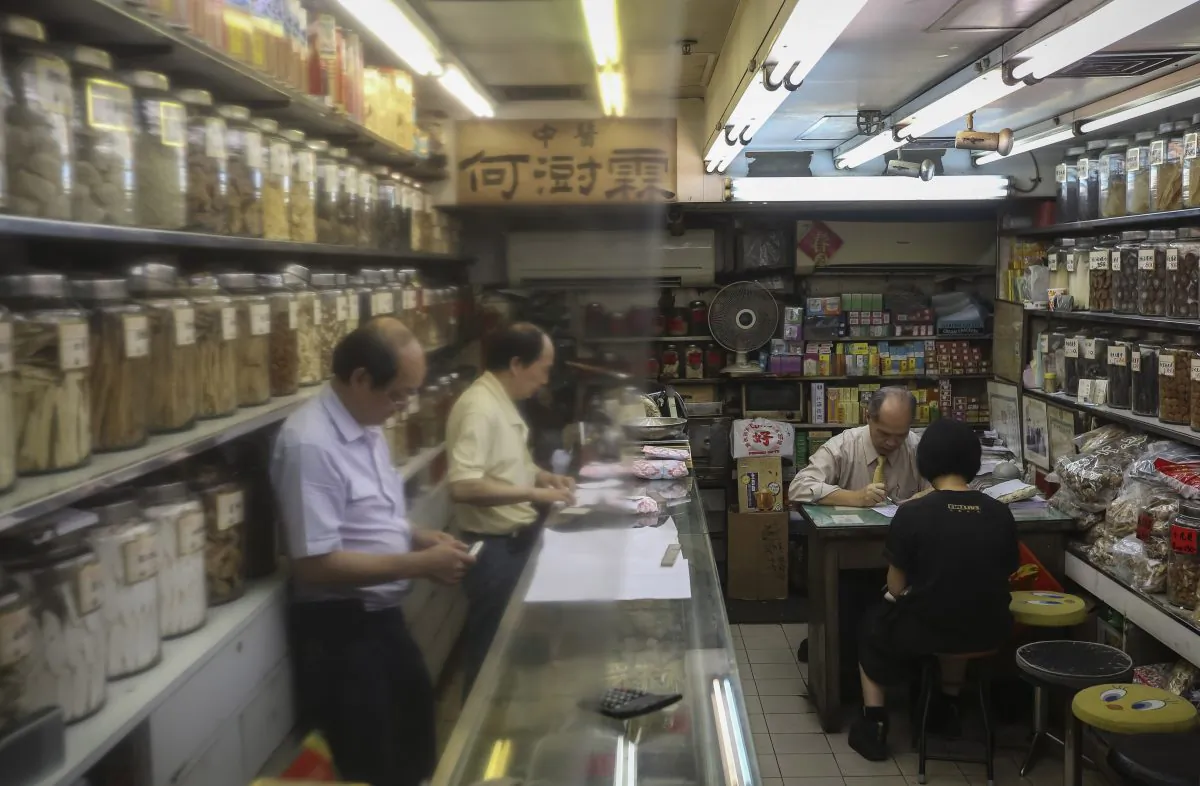 A traditional Chinese medicine practitioner (2nd-R) advises a client (R), as two others work at a counter inside a Chinese medicine shop in Hong Kong on July 7, 2018. (Vivek Prakash/AFP/Getty Images)