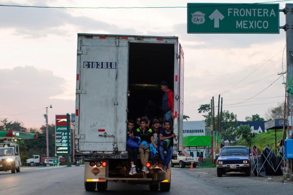 Immigrants pass by a highway sign that reads in Spanish: "Mexico Border", as they take a lift in the back of a truck during their journey towards the United States, in Pajapita, Guatemala