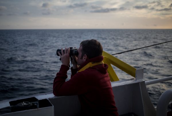One of the crew members of the Dutch-flagged rescue vessel Sea Watch 3 keeps a watch on the sea with binoculars