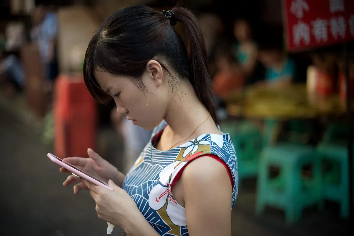A young woman looks at her smartphone in Chongqing City on Aug. 24, 2016. (NICOLAS ASFOURI/AFP/Getty Images)