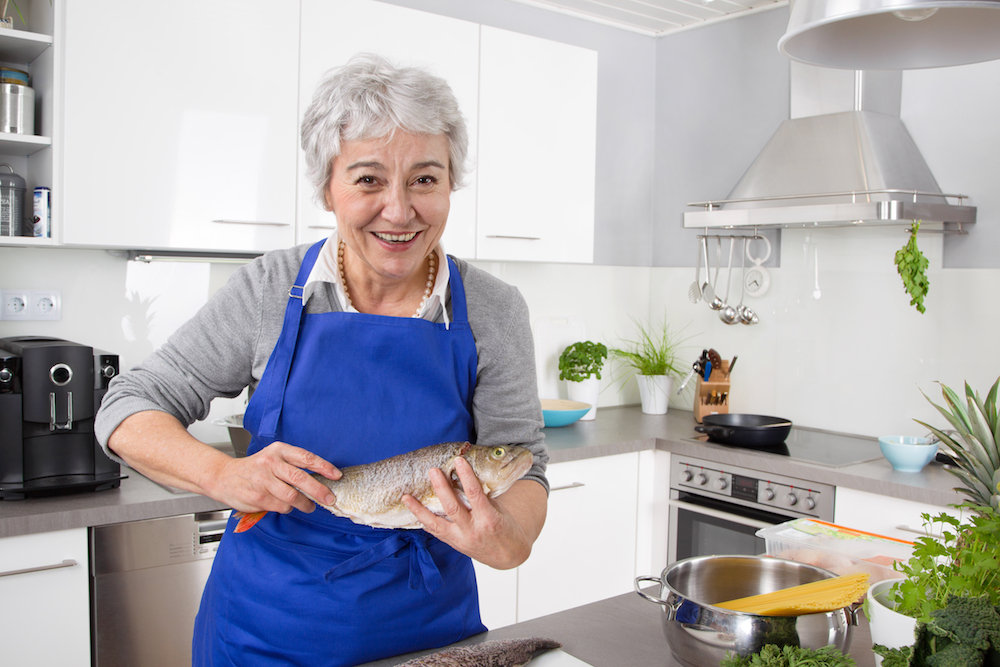 My grandmother usually cooks. Рыба на кухне. Хозяйка с рыбой. Пожилая женщина на кухне. Женщина готовит рыбу.