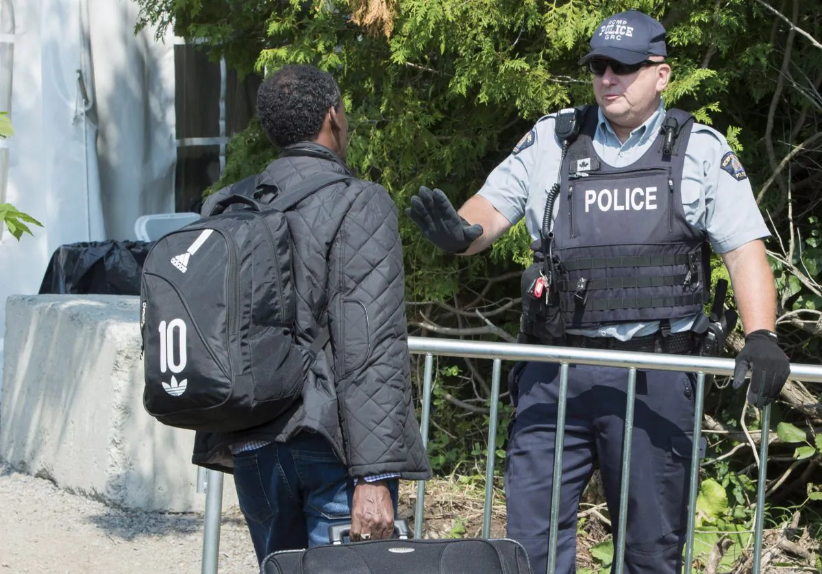 An asylum seeker is confronted by an RCMP officer as he crosses the border into Canada from the United States on Aug. 21, 2017 near Champlain, N.Y. (The Canadian Press/Paul Chiasson)