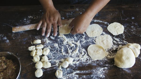 Hands roll out homemade dumpling dough on floured surface