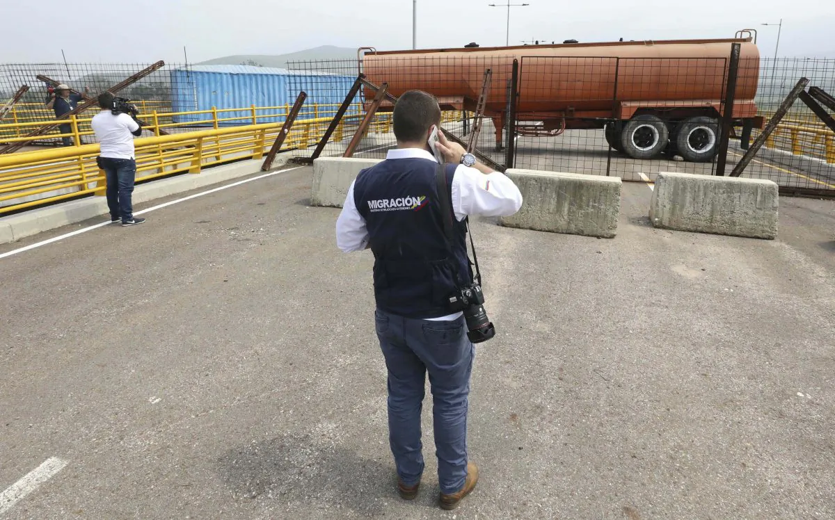 An immigration official observes a fuel tanker, cargo trailers, and makeshift fencing, used as barricades by Venezuelan authorities attempting to block humanitarian aid entering from Colombia on the Tienditas International Bridge that links the two countries as seen from the outskirts of Cucuta, Colombia, on Feb. 6, 2019. (AP Photo/Fernando Vergara)