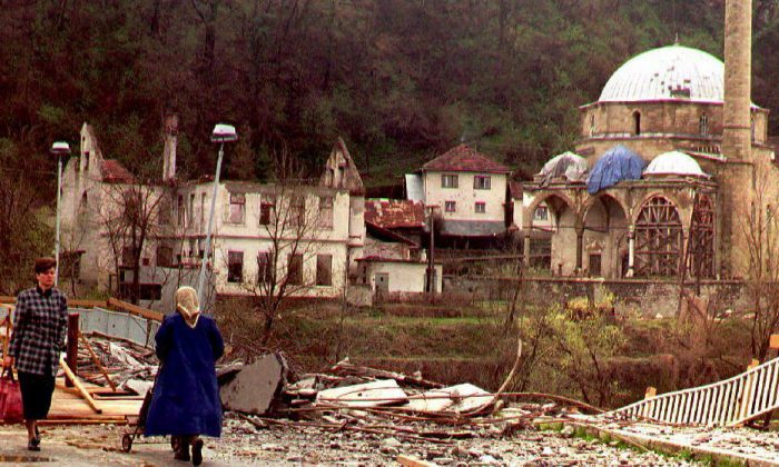 Two women pass a bridge, damaged by Serb artillery fire, to cross the Bosna river 27 March 1994. At right, the half-destroyed mosque of Maglaj. The siege of this mainly Moslem enclave was lifted last week. (Photo credit should read ERIC CABANIS/AFP/Getty Images)