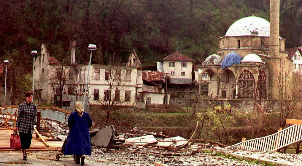Two women pass a bridge, damaged by Serb artillery fire, to cross the Bosna river 27 March 1994. At right, the half-destroyed mosque of Maglaj. The siege of this mainly Moslem enclave was lifted last week. (Photo credit should read ERIC CABANIS/AFP/Getty Images)