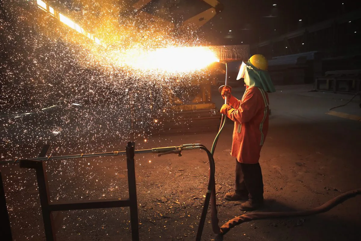 A worker trims a newly-cast steel slab at the NLMK Indiana steel mill in Portage, Indiana, on March 15, 2018. Chinese overproduction and dumping tactics lost thousands of jobs for the U.S. steel industry, say experts. (Scott Olson/Getty Images)