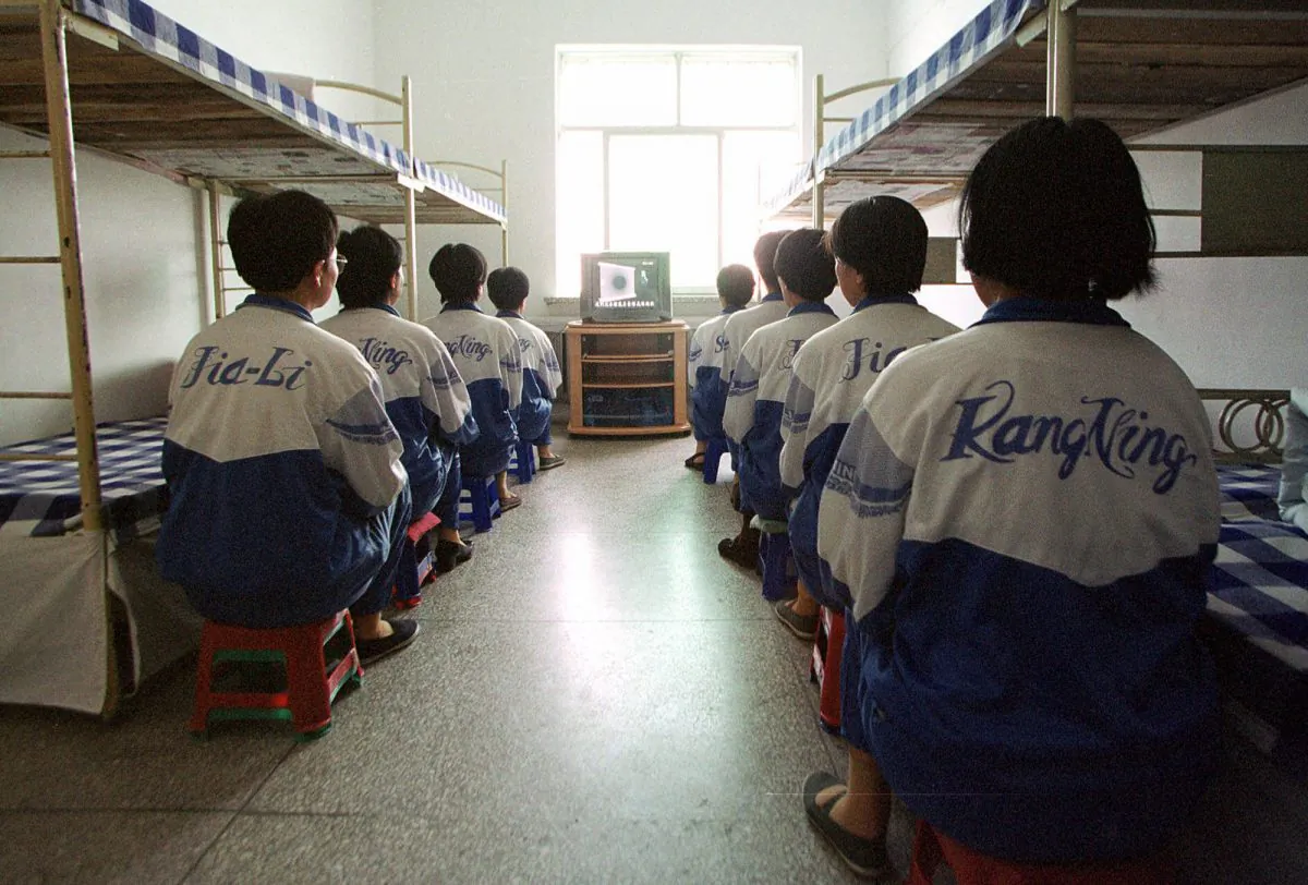 Falun Dafa practitioners are shown in Masanjia labour camp watching a video meant to “re-educate” them during a propaganda tour arranged by the camp authorities on May 22, 2001. One of the tortures used on the practitioners involves handcuffing them awkwardly between bunk beds, and then yanking the beds apart, causing excruciating pain. (AP Photo/John Leicester)