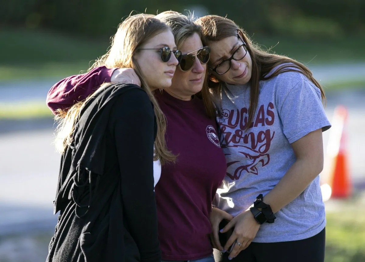Emma Rothenberg, left to right, with her mother Cheryl Rothenberg and sister, Sophia Rothenberg embrace at a memorial marking the one-year anniversary of a mass shooting at Marjory Stoneman Douglas High School in Parkland, Fla., on Feb. 14, 2019. (Al Diaz/Miami Herald via AP)