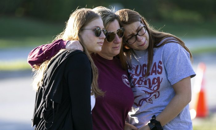 Emma Rothenberg, left to right, with her mother Cheryl Rothenberg and sister, Sophia Rothenberg embrace at a memorial marking the one-year anniversary of a mass shooting at Marjory Stoneman Douglas High School in Parkland, Fla., on Feb. 14, 2019. (Al Diaz/Miami Herald via AP)