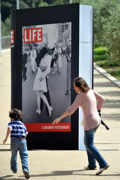 A People pass by a poster announcing the "Life. I grandi fotografi" (Life. The great photographers) exhibition with "VJ Day a Times Square,