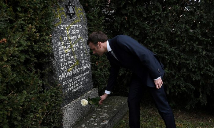 French President Emmanuel Macron lays a white rose on a grave vandalised with swastikas during a visit at the Jewish cemetery in Quatzenheim, France on Feb. 19, 2019. (Frederick Florin/Pool via Reuters)