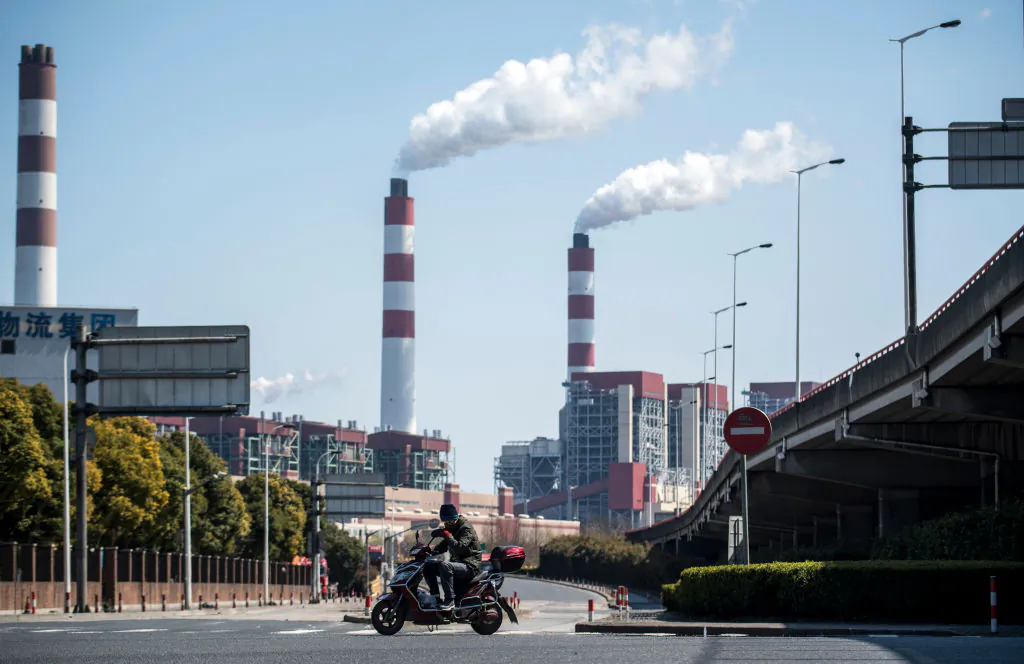 A man rides his scooter near the Shanghai Waigaoqiao Power Generator Company coal power plant in Shanghai on March 6, 2017. (JOHANNES EISELE/AFP/Getty Images)