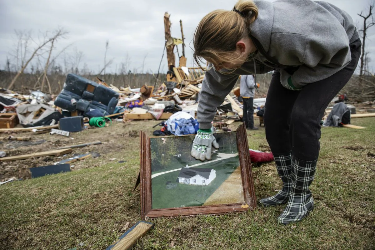Debris from a friend's home stands in the background as Ashley Griggs wipes away dirt from a photo found in the rubble of what it used to look like before it was destroyed by a tornado in Beauregard, Ala., on March 4, 2019. (David Goldman/AP Photo)