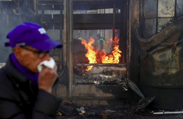 A man covering his face walks past a burning newsagent's shop