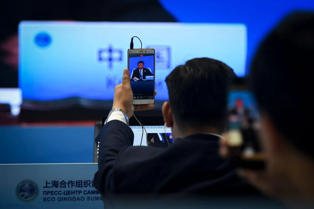 A journalist uses his mobile phone to broadcast live footage as a giant video screen (background) shows Chinese leader Xi Jinping speaking during Shanghai Cooperation Organisation Summit in Qingdao, China's Shandong Province on June 10, 2018. (Wang Zhao/AFP/Getty Images)