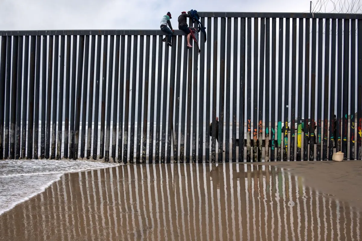 Central American migrants sit above the US-Mexico border fence as a Border Patrol agent stands guard, as seen from Tijuana to San Diego  as seen from Playas de Tijuana, in Baja California state, Mexico, on March 21, 2019.  (Guillermo Arias/AFP/Getty Images)