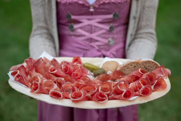 Girl holds platter of Italian speck with bread and pickles