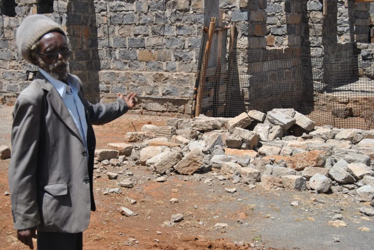 Peter Muchiri points at his neighbor's wall that collapsed following vibrations from blasts at the quarry near Kanairobi village, Kenya, on March 28, 2019. (Dominic Kirui for The Epoch Times)