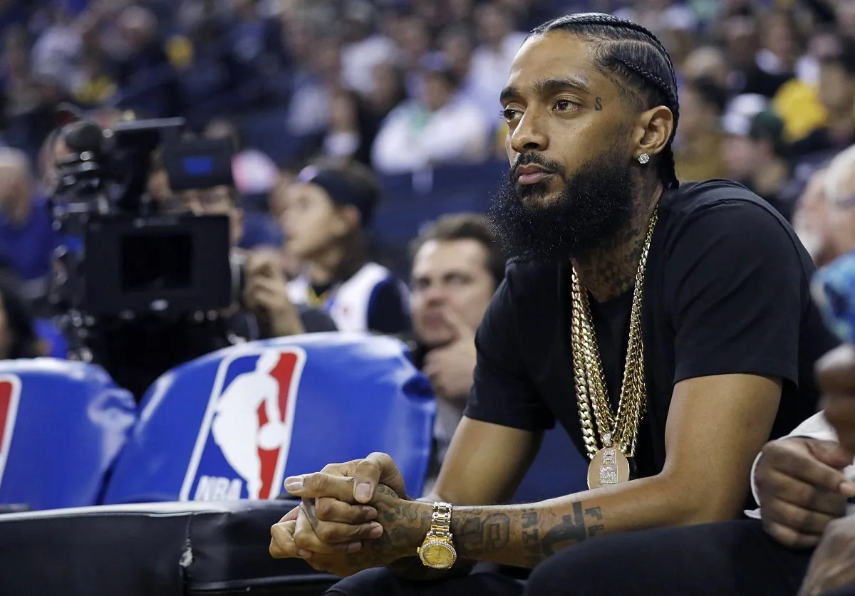 The rapper Nipsey Hussle watches an NBA basketball game between the Golden State Warriors and the Milwaukee Bucks in Oakland, Calif., on March 29, 2018. (Marcio Jose Sanchez/AP Photo)
