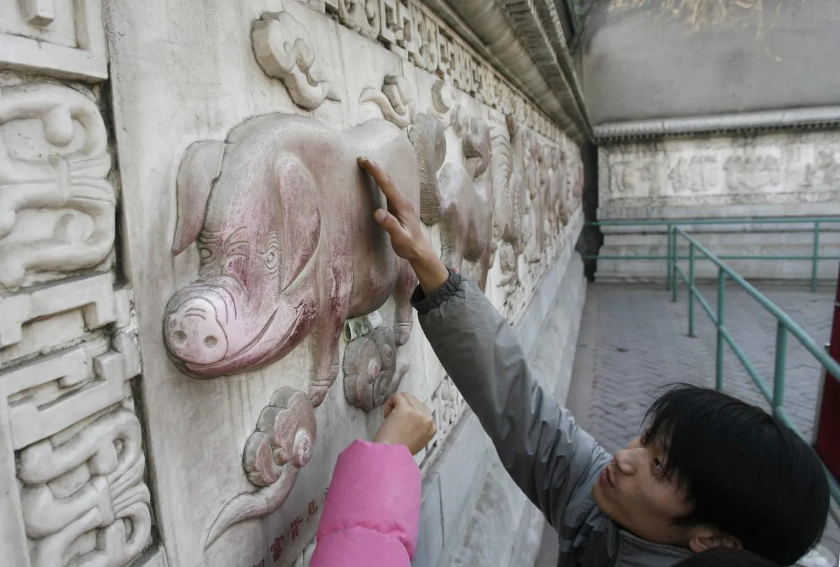 A man touches a pig on a wall of bas relief sculptures of the twelve animals in the lunar calendar, at the White Cloud Temple in Beijing on Feb. 15, 2007. On Feb. 5, 2019, the Year of the Pig began, marked by disturbing economic news for China. (Frederic J. Brown/AFP/Getty Images)