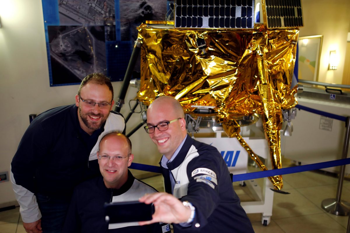 Members of Israeli non-profit group SpaceIL and representatives from Israel Aerospace Industries (IAI) do a selfie in front of a model of Beresheet spacecraft, near the control room, in Yahud