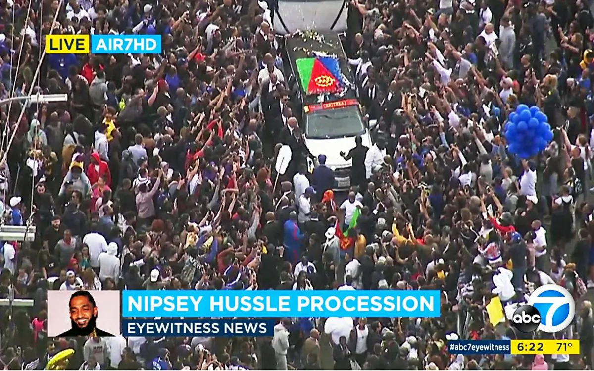 This photo taken from video provided by ABC7 shows thousands of people reaching towards the hearse carrying the body of rapper Nipsey Hussle in South Los Angeles on April 11, 2019. (ABC7 via AP)