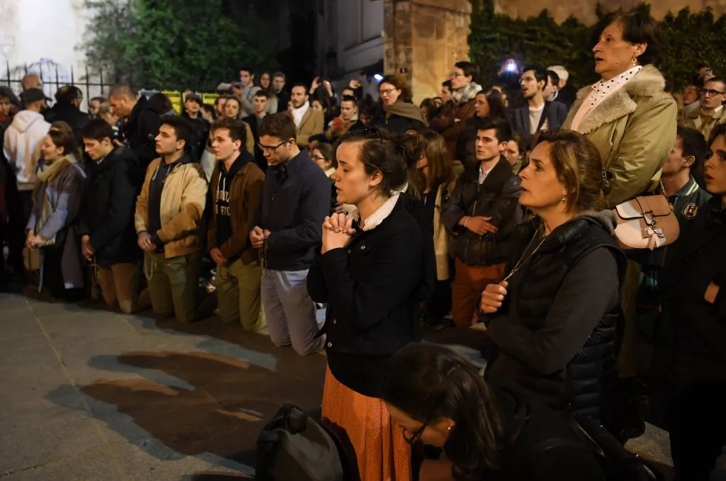 People kneel on the pavement as they pray outside watching flames engulf Notre-Dame Cathedral in Paris on April 15, 2019. (ERIC FEFERBERG/AFP/Getty Images)