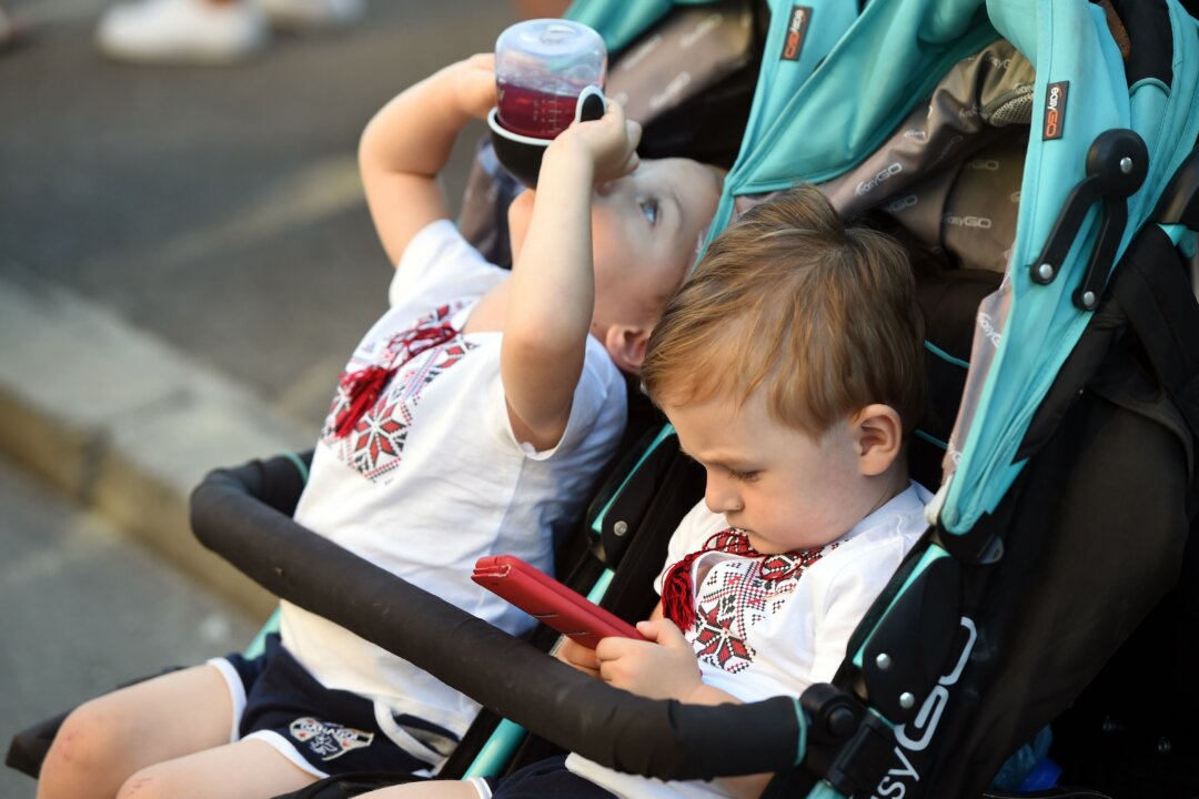 A toddler plays with a mobile phone while his twin brother drinks juice at an event in Kiev, on Aug. 11, 2018. (Sergei Supinsky/AFP/Getty Images)
