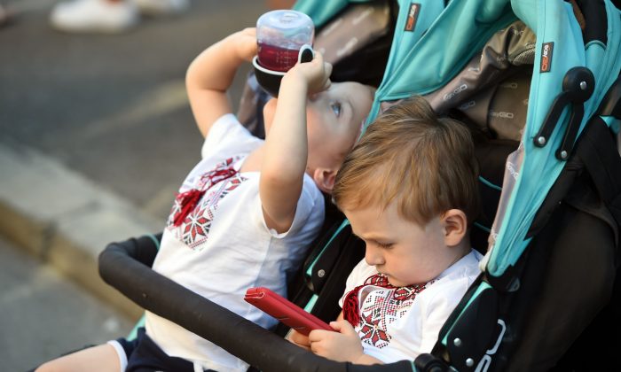 A baby plays with a mobile phone while his twin brother drinks juice in Kyiv, Ukraine,  on Aug. 11, 2018. (Sergei Supinsky/AFP/Getty Images)
