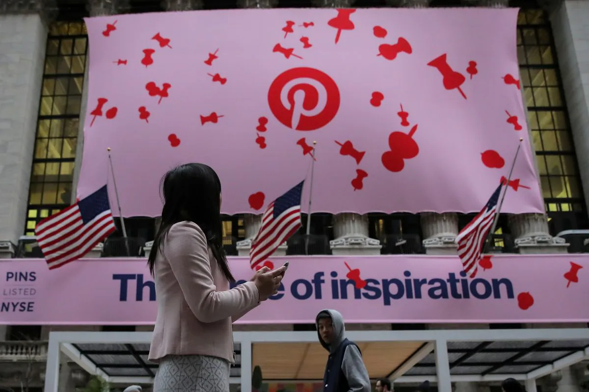 A woman uses her phone as a banner celebrating the IPO of Pinterest Inc. hangs on the front of the New York Stock Exchange in New York, on April 18, 2019. (Brendan McDermid/Reuters)