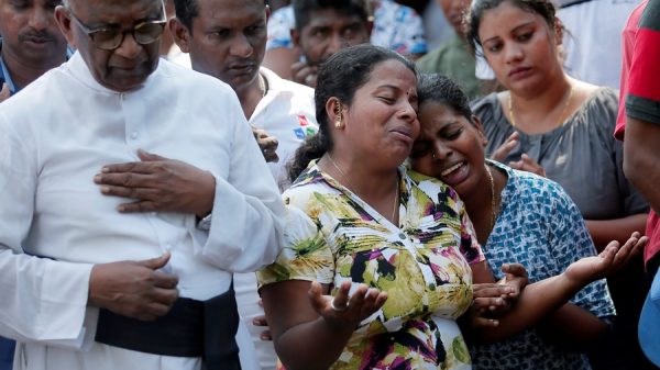 People react during a mass burial of victims
