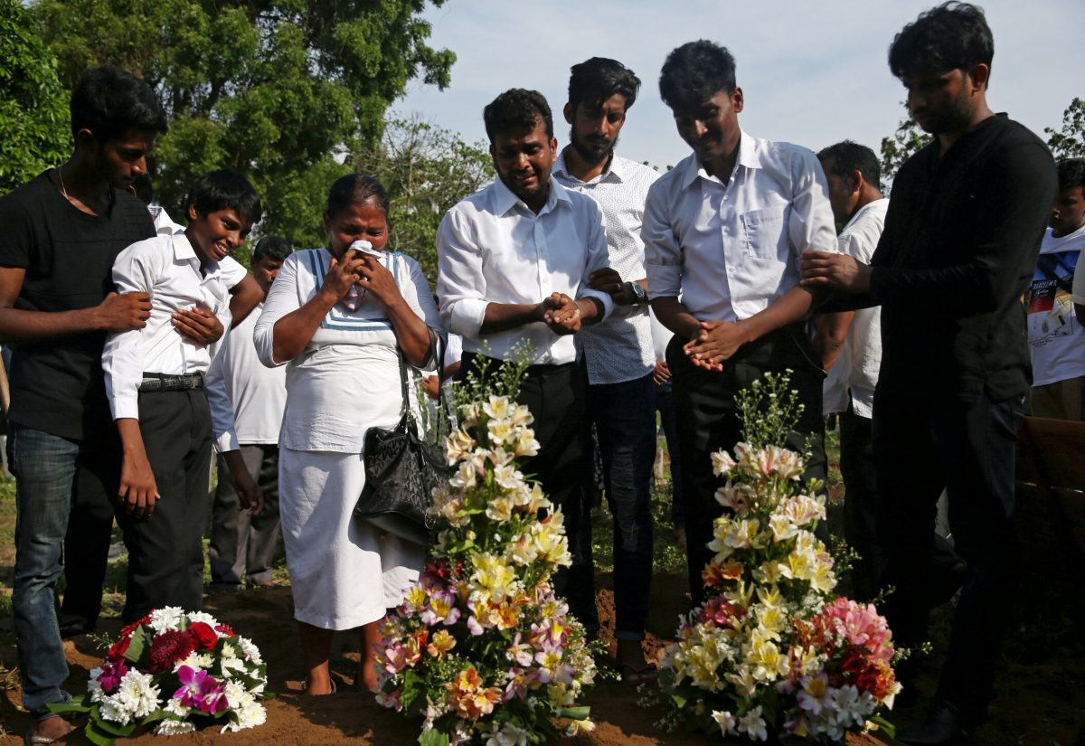 People react during a mass burial of victims