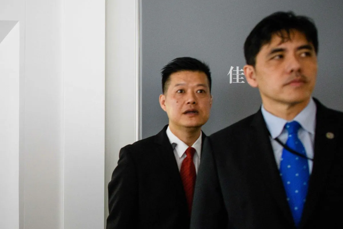 This picture taken on October 13, 2017, shows a man (R, wearing blue tie) identified by local Hong Kong media as former CIA agent Jerry Chun Shing Lee standing in front of a member of security at the unveiling of Leonardo da Vinci's 'Salvator Mundi' painting at the Christie's showroom in Hong Kong. (Anthony Wallace/AFP/Getty Images)