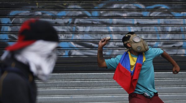 An anti-government protester winds up to throw a rock