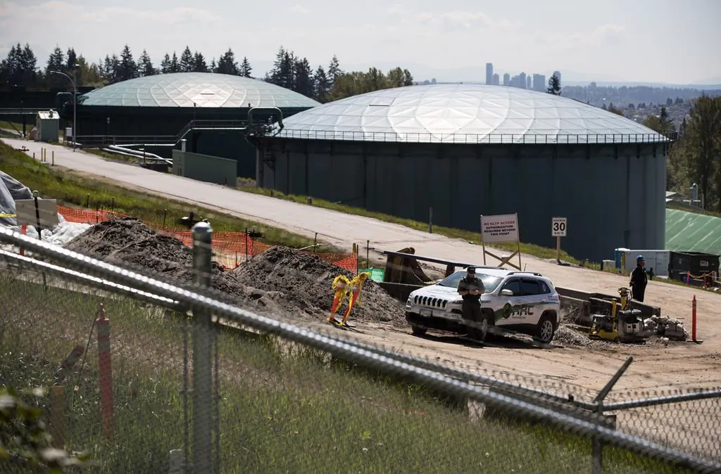 A security guard stands nearby construction workers at the Kinder Morgan Burnaby Terminal tank farm, the terminus point of the Trans Mountain pipeline, in Burnaby, B.C., on April 30, 2019. (Darryl Dyck/The Canadian Press)