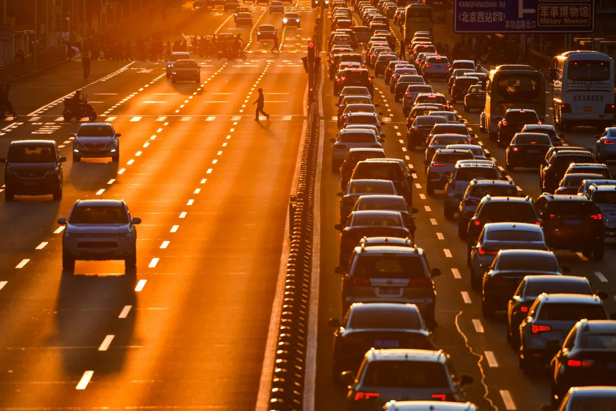 A pedestrian walks on a crossing next to cars in the traffic on a main road during sunset. (Reuters)