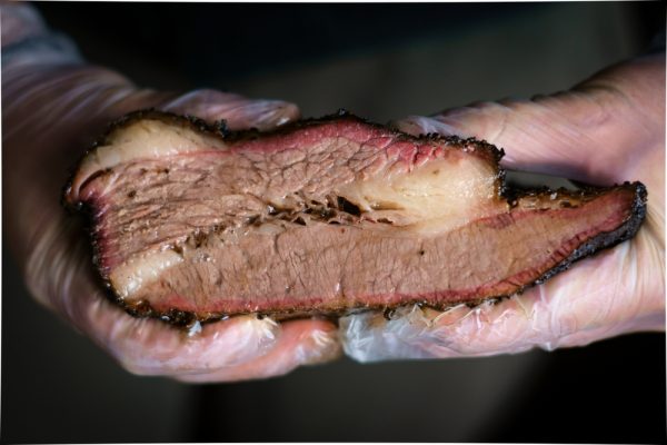 gloved hands hold cut texas barbecued brisket