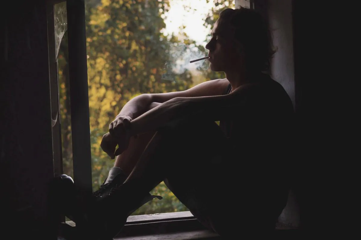 A man sits by a window smoking. (fjord77/Pixabay)