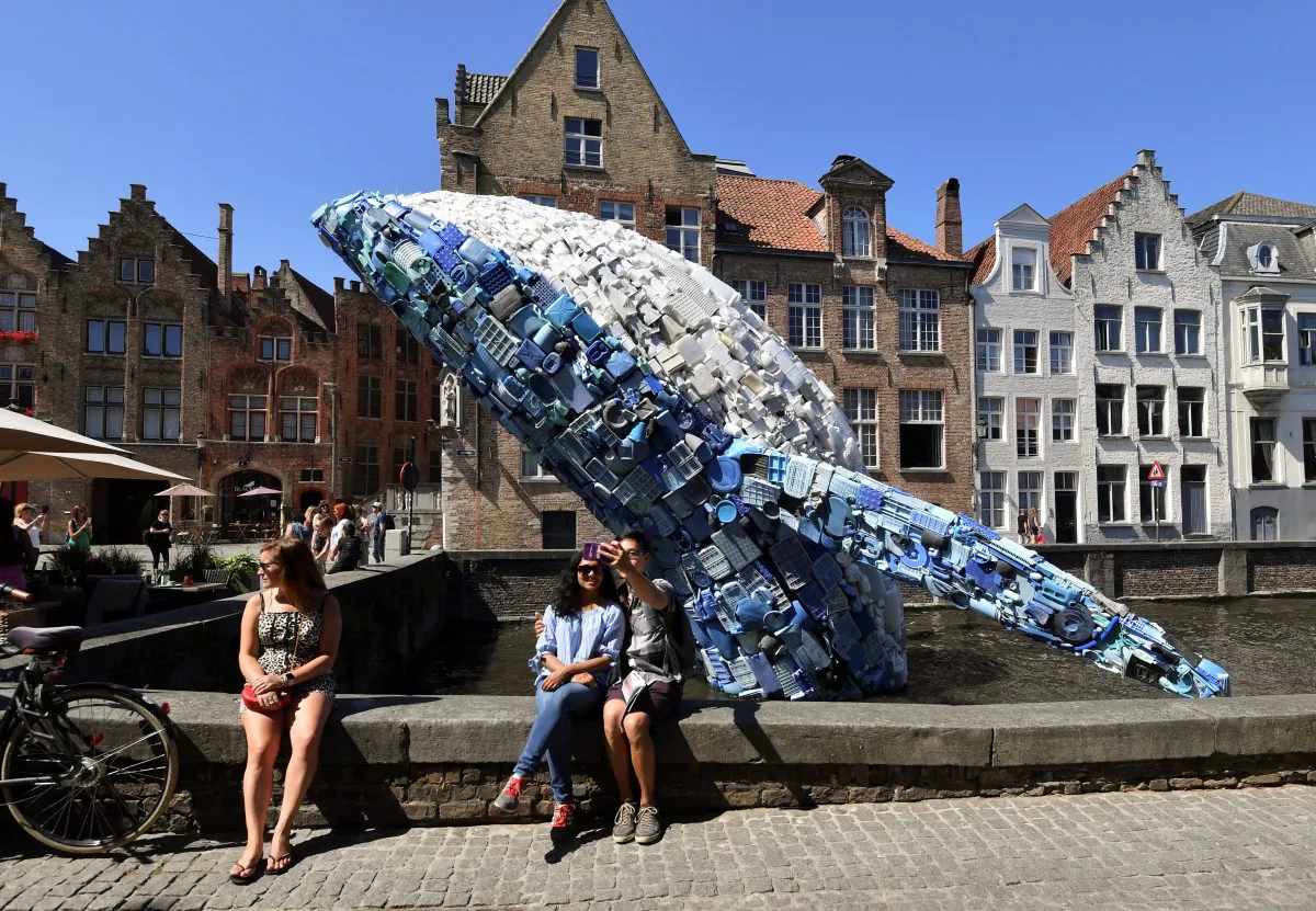 Tourists pose for a selfie picture with a 12-metre installation depicting a whale, made up of five tons of plastic waste pulled out of the Pacific Ocean, displayed in Brugges, on July 14, 2018 for the 2018 Bruges Triennial. (John Thys/AFP/Getty Images)