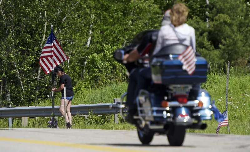 A motorcycle passes as a woman leaves flowers at the scene of a fatal accident on Route 2 in Randolph, N.H., on June 22, 2019. (Paul Hayes/Caledonian-Record via AP)