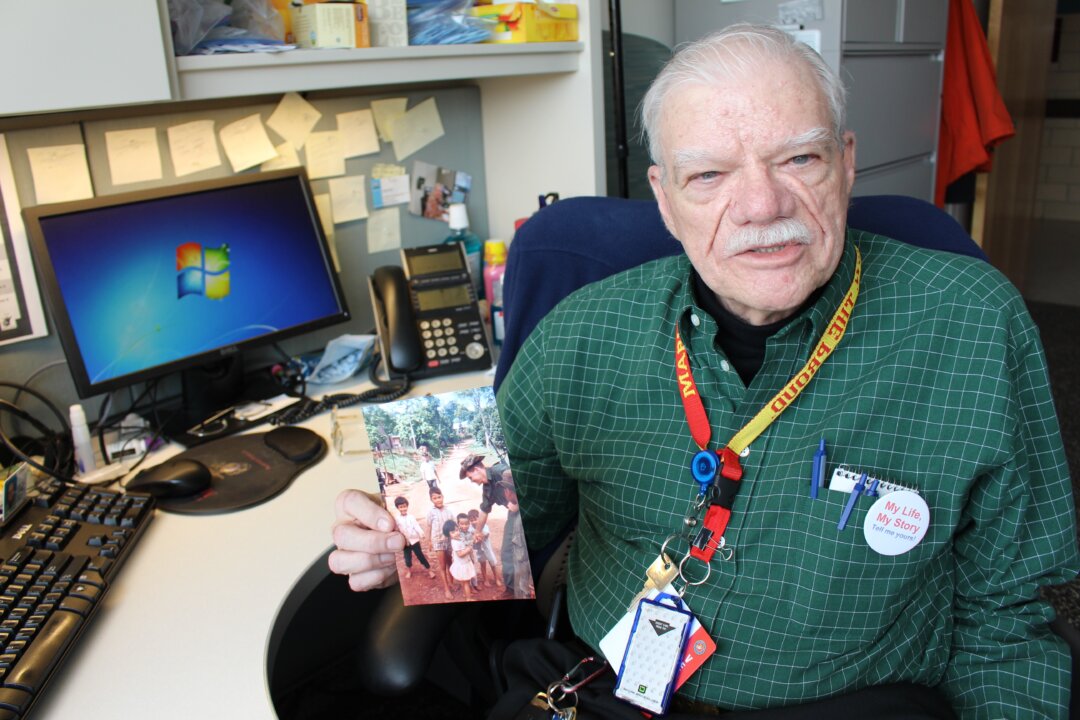 Bob Hall holds a photograph of himself playing with children in a village in Vietnam during his time as a Marine. Hall was one of the earliest patients to be interviewed for the My Life, My Story program. Now he is one of the program’s writers. (Bram Sable-Smith for NPR)