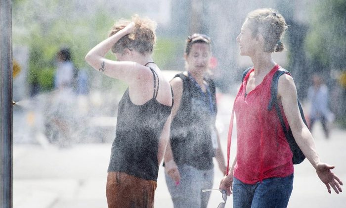 People use misters to cool down during a heatwave in Montreal, on July 2, 2018. Montreal's mayor is unveiling the city's plan to respond to heatwaves after dozens of people died amid high temperatures last summer. (Graham Hughes/The Canadian Press)