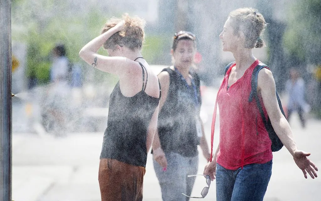 People use misters to cool down during a heatwave in Montreal, on July 2, 2018. Montreal's mayor is unveiling the city's plan to respond to heatwaves after dozens of people died amid high temperatures last summer. (Graham Hughes/The Canadian Press)