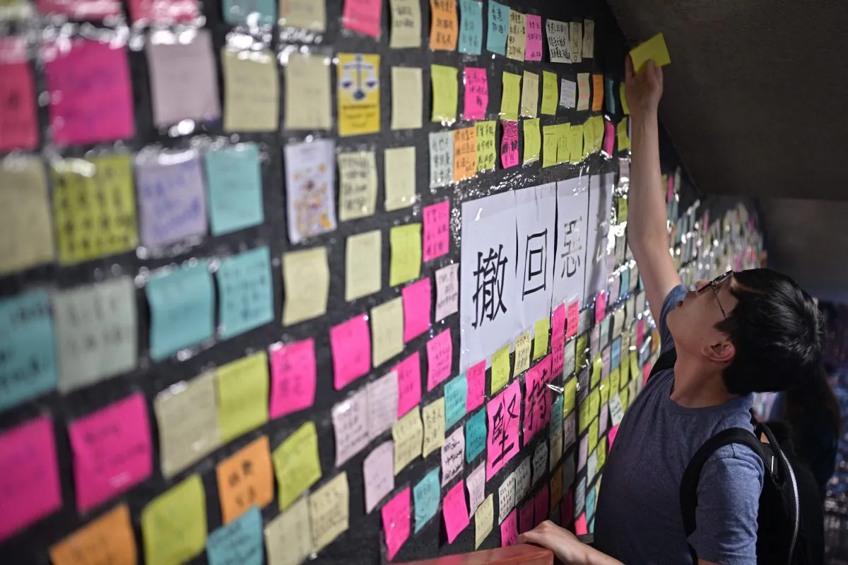 A man reaches up to place a handwritten note onto a makeshift "Lennon Wall" near a footbridge in Hong Kong on July 11, 2019. (Anthony WALLACE/AFP/Getty Images)