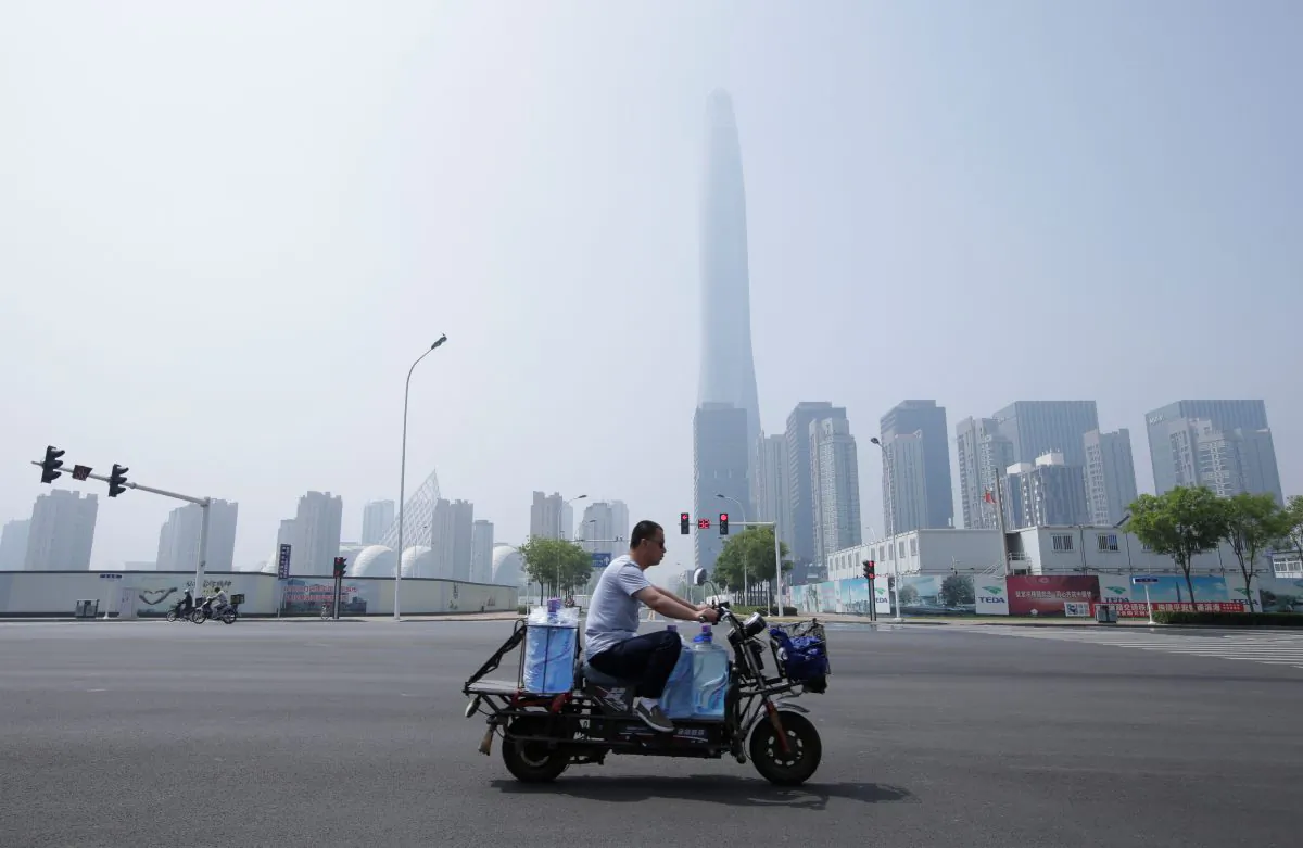 A man rides an electric motorcycle carrying water past Chow Tai Fook Financial Center in Tianjin's Binhai new district, China on May 16, 2019. (Jason Lee/Reuters)