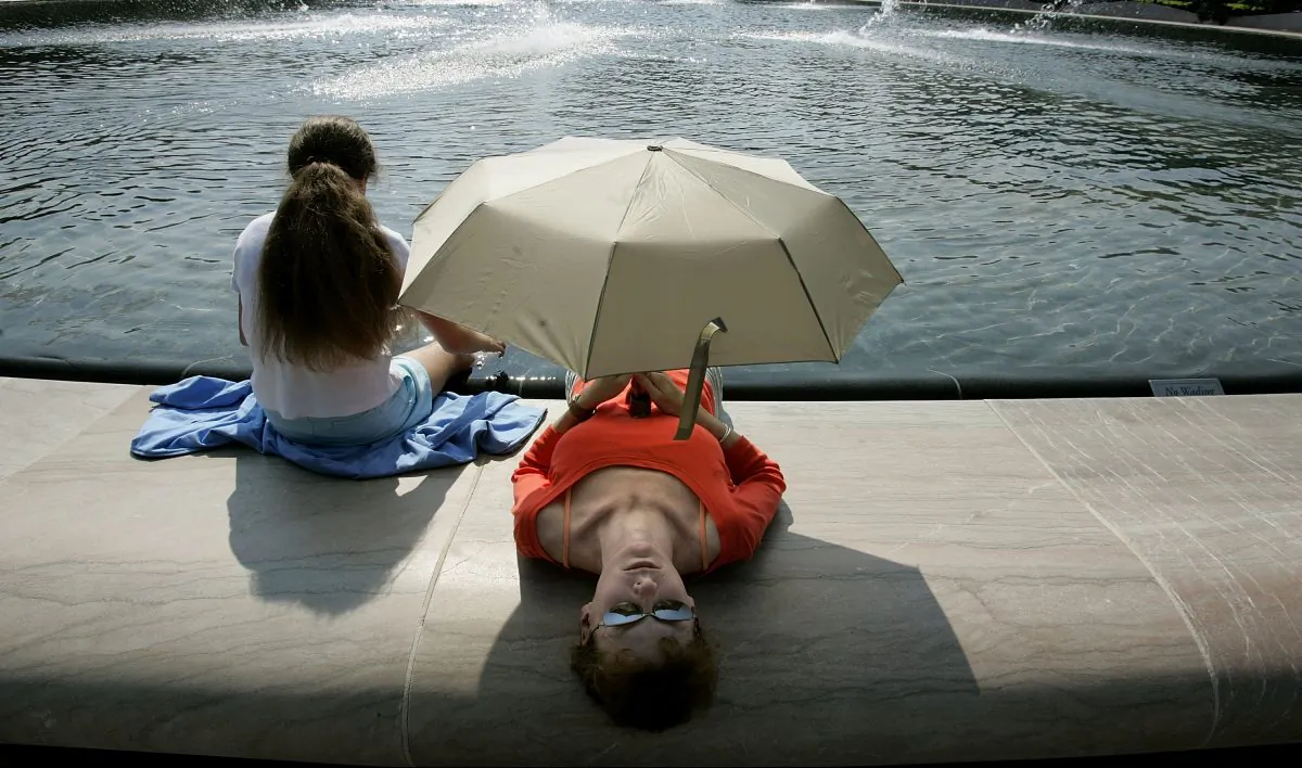 Paige Rose, 12 years-old, and her mother, Cindy Rose, of St. Louis, MO, take shade under an umbrella while they dip their feet in the fountain in the center of the National Gallery of Art Sculpture Garden in Washington on July 26, 2005. (Chip Somodevilla/Getty Images)