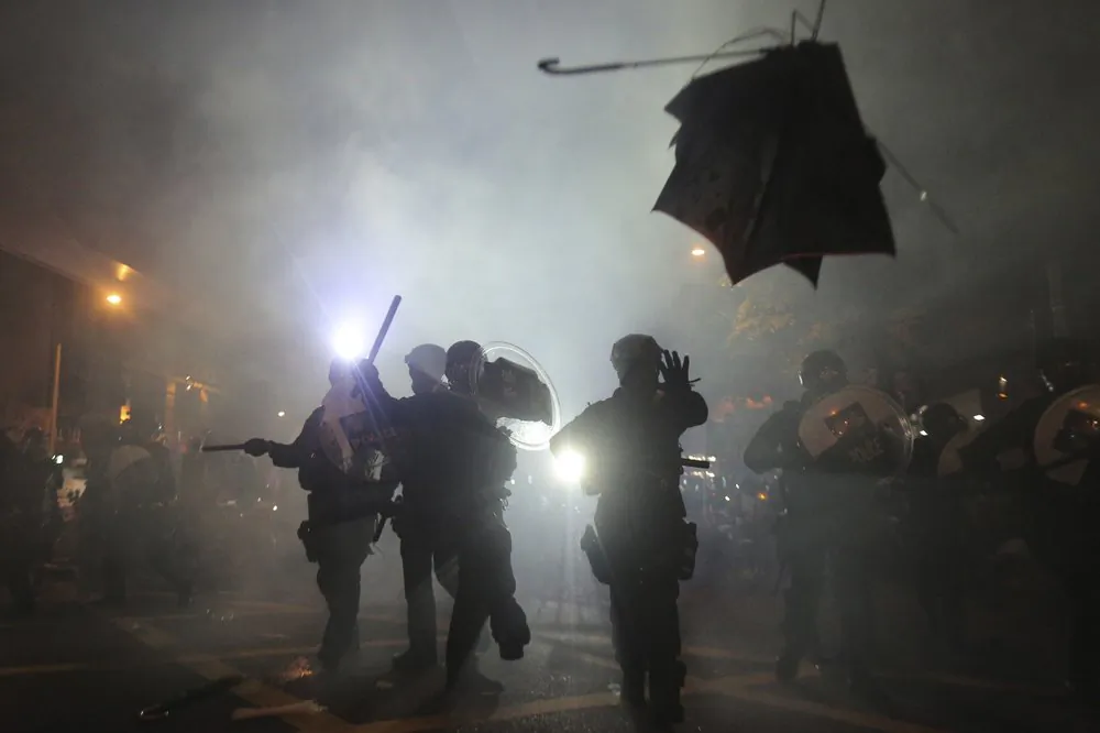 A broken umbrella flies by near riot police, during confrontation with protesters in Hong Kong on July 21, 2019. (Andy Lo/HK01 via AP)