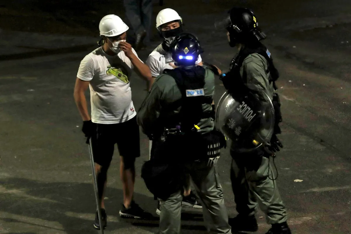 Men in white T-shirts and carrying poles talk to riot police in Yuen Long after attacking anti-extradition bill demonstrators at a train station in Yuen Long, Hong Kong on July 22, 2019. (REUTERS/Tyrone Siu)